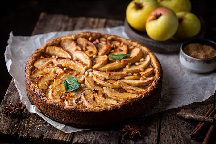 An apple tart on a wooden table beside a bowl of apples