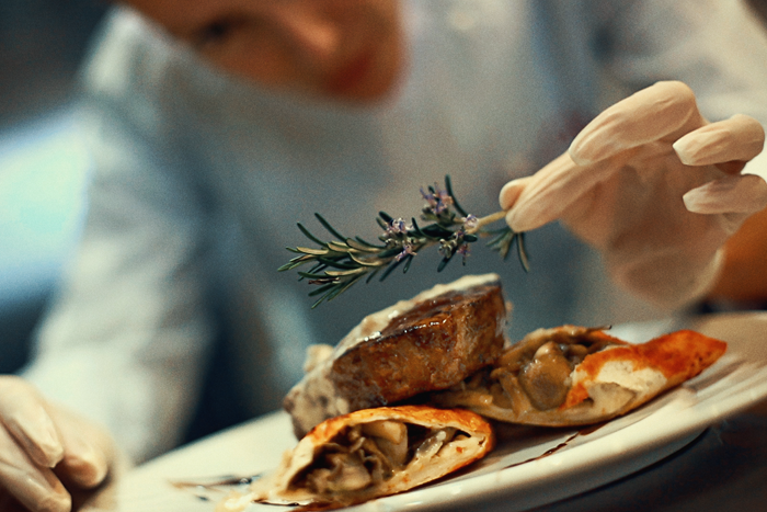 A closeup of a chef placing garnish on steak.