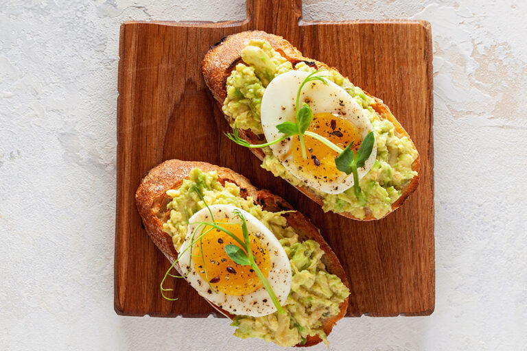 Avocado toast with hard boiled egg on a wooden board.