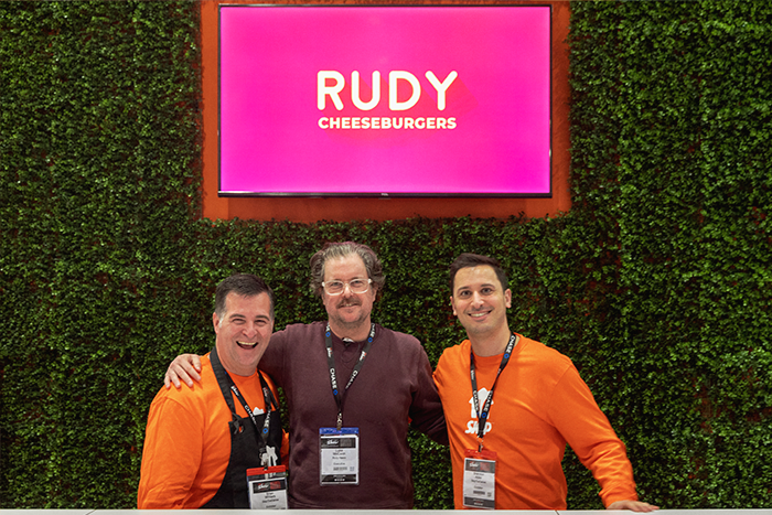 Rudy co-founder, Luke McCann, smiling with two Skip team members in Skip’s booth on day 1 of the 2023 RC Show.