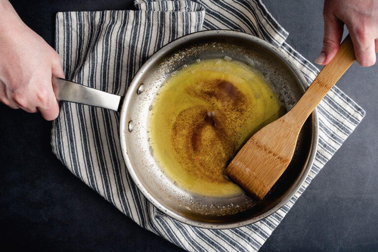 Une personne qui fait dorer du beurre en remuant dans une casserole en acier inoxydable.